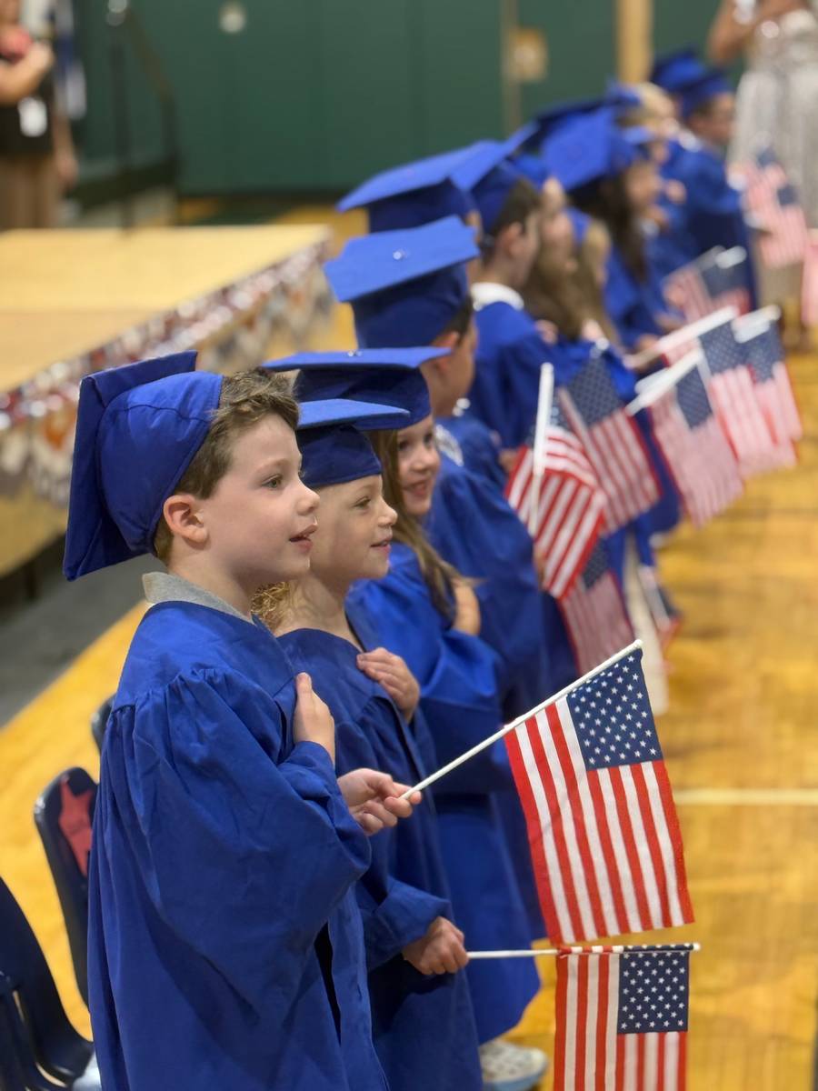 Humpty Dumpty Pre-K graduates in caps and gowns holding American flags